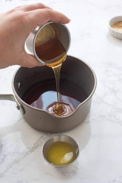 pouring honey into a saucepan with soy sauce already in pan